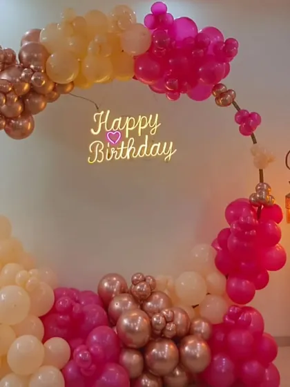 A circular balloon arch is a popular choice for creating a beautiful focal point. Here, a mix of rose gold, pink, and peach balloons with a "Happy Birthday" neon sign creates an elegant and picture perfect spot for any birthday celebration.