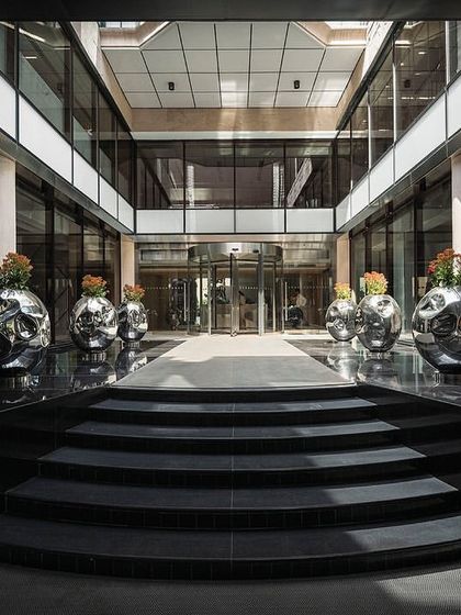 The grand entrance to The Layered Office features a new canopy and revolving door leading into an open-air courtyard, with black granite steps creating a formal approach.