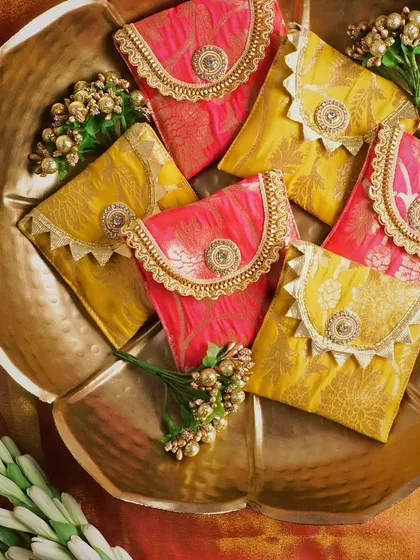 These festive Indian pouches are styled in a beautiful brass bowl, creating a sense of luxury and occasion. The rich colors of the fabric pop against the golden tones of the bowl and flowers.