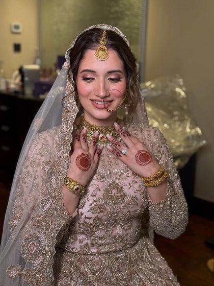 A happy, smiling portrait of the Nikkah bride. Her makeup is kept soft and radiant to complement her intricately embroidered golden outfit, proving that you don't need bold colors to make a statement.