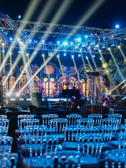 A wide shot of the Sangeet stage, with its intricate backdrop of illuminated windows and dramatic spotlights, ready for a grand show.