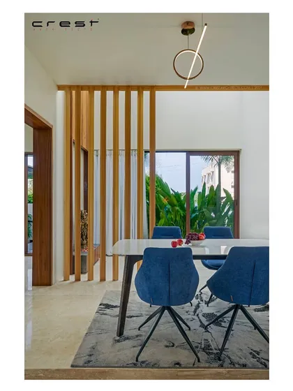 The dining space in the 'Framed House' combines cool blue chairs with the warmth of timber screens and natural light. The design creates a fresh, calm atmosphere perfect for family meals.