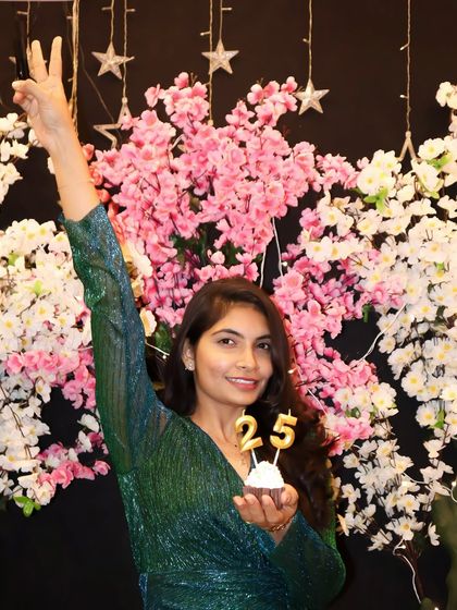 Celebrating 25 with a cupcake and a victory sign. The floral backdrop adds a touch of elegance to this milestone birthday celebration.