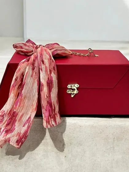 A chic and reusable red gift trunk, perfect for any special occasion. It features a stylish scarf tied as a bow, adding a fashionable touch to the gift presentation.