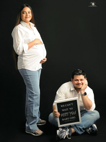 A fun and sweet studio portrait with a sign that reads, "We can't wait to meet you baby girl." The simple black background makes the couple's joy the center of attention.