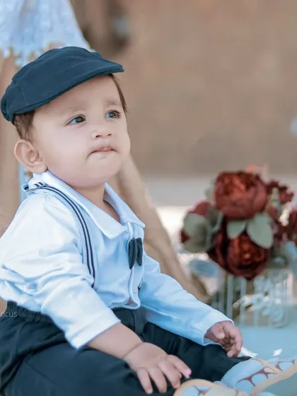 A dapper little boy dressed in a newsboy cap and suspenders enjoys a picnic setup on the sand. We can bring our creative props to any location.