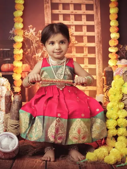 A beautiful portrait of a toddler dressed as Radha, holding a flute. The rich colors of her dress and the traditional backdrop create a stunning image.