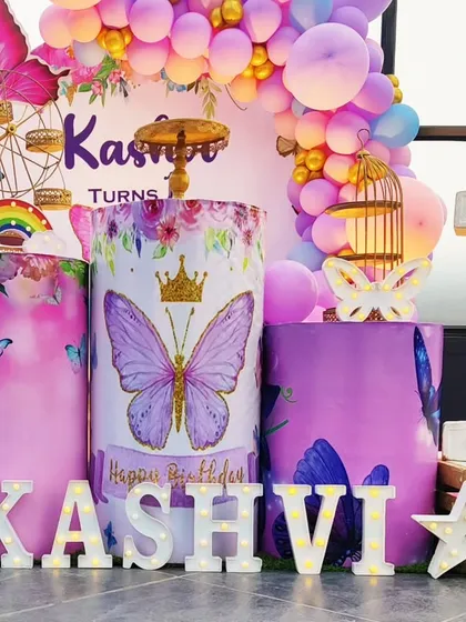 A detailed shot of a butterfly-themed first birthday, showing the custom-printed plinths and 'KASHVI' marquee letters.