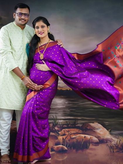 A beautiful full-length portrait of the couple in traditional Indian outfits. The flowing saree and coordinated clothing create a regal and timeless image against a painted backdrop.