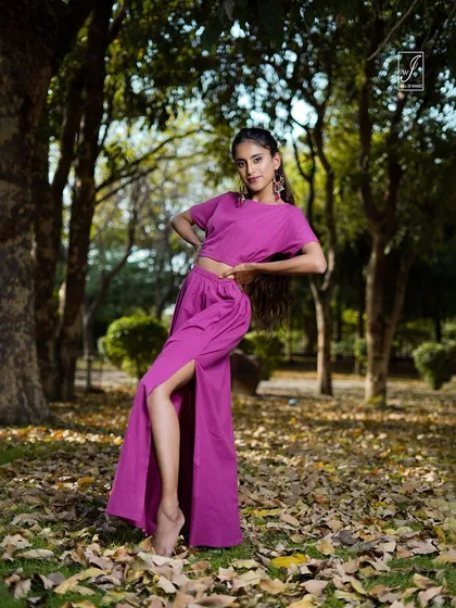 A dynamic pose in a forest setting, with the model in a vibrant magenta two-piece outfit. The slit in the skirt adds a touch of drama and movement.
