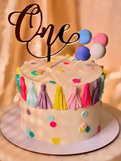 A festive and colorful cake for a first birthday party. This lemon-flavored cake is decorated with a fun tassel garland, confetti dots, and a balloon topper.