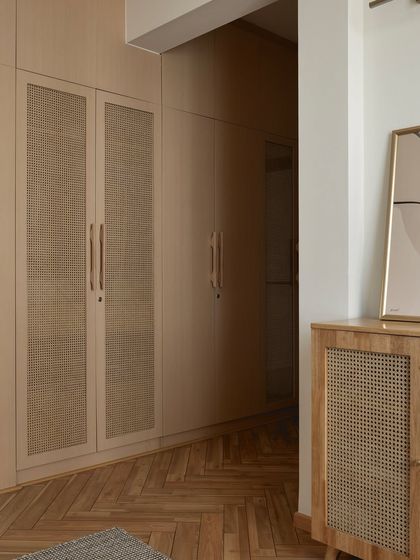 The walk-in closet in this Japandi-style master bedroom features full-height wardrobes with a light wood and cane finish, creating a warm, organized, and serene space.