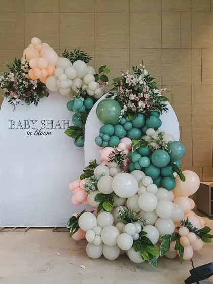 A chic "Baby Shah in Bloom" decoration with a unique color palette. The mix of sage green, peach, and white balloons, combined with fresh flowers and leaves, offers a fresh and modern aesthetic.