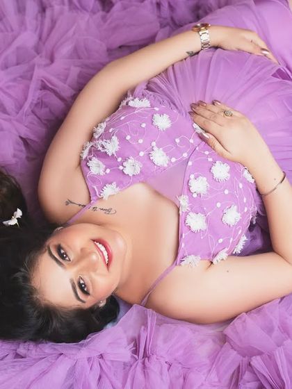 A joyful overhead portrait. Lying on a bed of purple tulle, this mother-to-be's bright smile and henna-adorned hands create a beautiful and happy image.