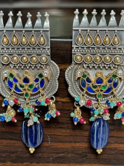 These top-notch silver fusion earrings are back in stock. They feature a crown-like silver top, gold-plated accents, and a colourful enamel peacock motif with dangling blue beads.
