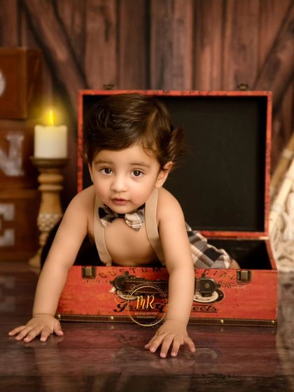 A curious one-year-old peeking out of a vintage-style suitcase during his rustic-themed birthday photoshoot.
