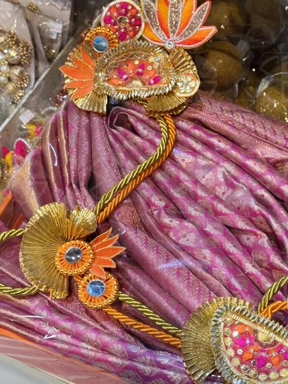 A rich purple Banarasi saree, beautifully folded and decorated with traditional gota art. I ensure the packing complements the richness of the fabric, making it a truly royal gift.