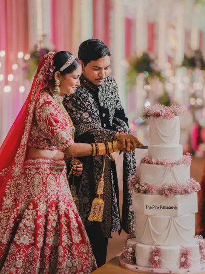 A beautiful moment captured as the happy couple cuts into their five-tiered classic white wedding cake. The cake is elegantly decorated with swags of delicate pink flowers, making it a timeless choice for a grand wedding.