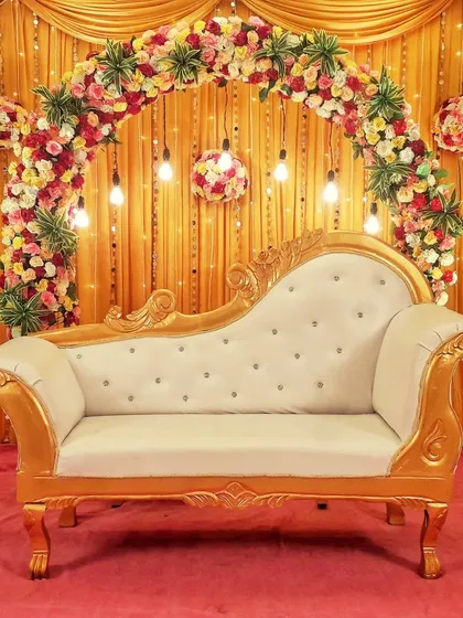 A simple yet elegant stage backdrop featuring a floral arch over an ornate golden-framed divan, suitable for engagements or as a photo booth.