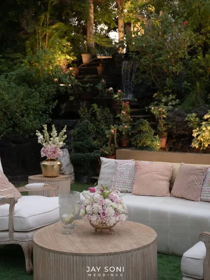 A serene lounge area set against a natural waterfall backdrop. The comfortable white seating and soft pink cushions create a tranquil space for guests to relax and enjoy the beautiful surroundings.