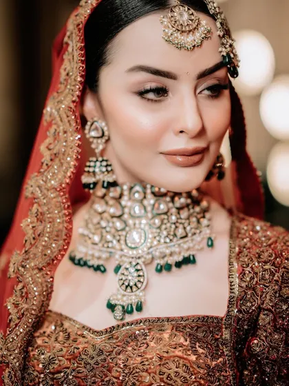 A close-up of a bride's regal look, featuring a heavy polki and emerald choker with a matching passa and tikka.
