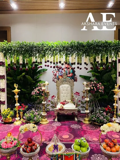 A complete Seemantham (baby shower) setup. This traditional arrangement features a backdrop of fresh banana leaves and jasmine strings, a decorated chair for the mother-to-be, and brass lamps, all surrounded by floral offerings.