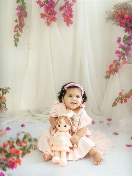 A wide shot of the beautiful ten-month milestone setup, featuring a baby girl and her doll surrounded by pink flowers and soft drapes.