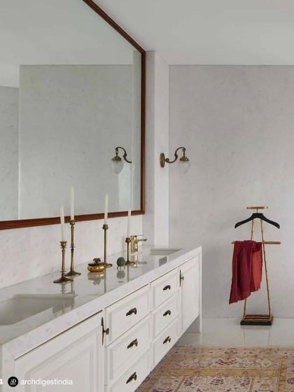 This image from an Architectural Digest feature shows the master bathroom's double vanity. The clean white cabinetry, classic marble, and vintage-style brass fittings create a look of understated luxury that is both timeless and functional.