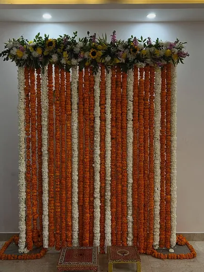 A simple and elegant photo backdrop or pooja setup made entirely of orange and white marigold strings.