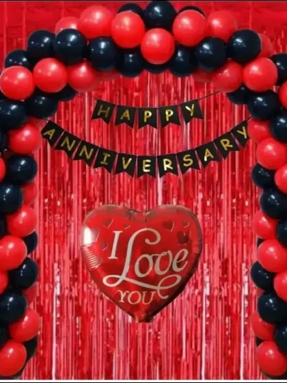 A classic anniversary decoration for an at-home celebration. This setup includes a red and black balloon arch over a red fringe curtain, with an 'Happy Anniversary' banner and a large 'I Love You' heart balloon.