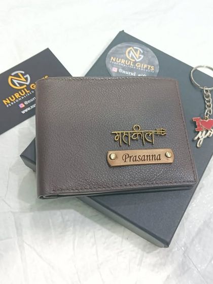 A brown leather wallet personalized with a name in Hindi script, shown with its gift box and a bonus keychain.