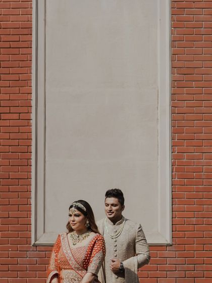 A modern, architectural portrait of the couple against a brick wall. The clean lines and simple background put all the focus on them and their stylish wedding attire.