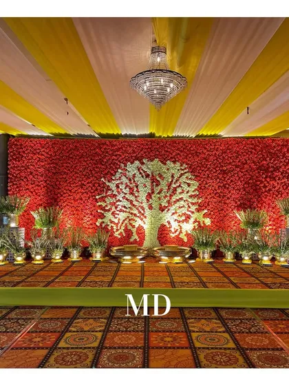 A unique Haldi stage backdrop featuring a 'Tree of Life' made entirely of white and green flowers, set against a dense wall of red florals.