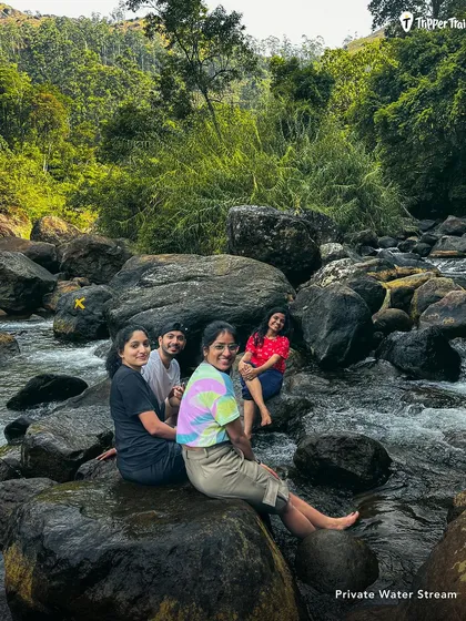 A group of friends sits on rocks in a private water stream in Munnar. I find these exclusive, offbeat spots for you to enjoy nature without the crowds.