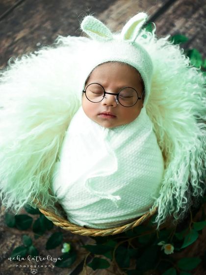 The little scholar again. This baby looks adorable in a bunny bonnet and tiny round glasses, creating a playful and memorable portrait.