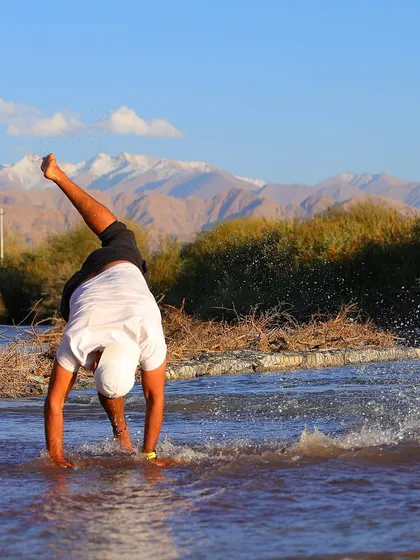 Fitness should also be fun. Here, one of our team members celebrates with a playful cartwheel in the cool river water after a tough day of training, with the beautiful mountains of Ladakh in the background.