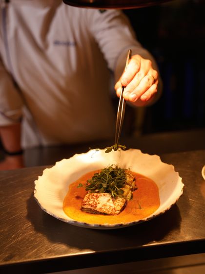 Our chef carefully plates a dish with tweezers, adding a final garnish. This action shot highlights the meticulous attention to detail that defines our culinary philosophy.