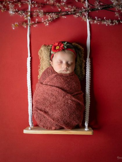 Dreaming sweetly on a tiny swing. The bold red background and delicate cherry blossoms make this a striking and beautiful image, with the baby safely and comfortably swaddled.