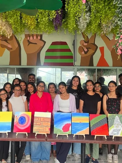 A group photo from a "Paint & Express" workshop, with everyone displaying their diverse and colorful canvases.