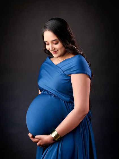 A classic solo maternity portrait in a royal blue gown. The focus is on the beautiful silhouette and the mother's loving gaze towards her baby bump.