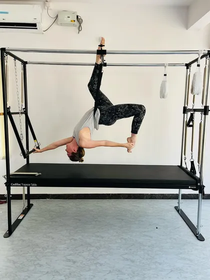This advanced aerial pose on the Cadillac requires a high degree of flexibility, balance, and core control.