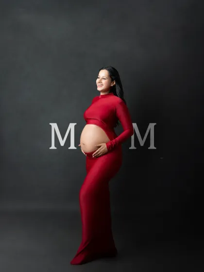 Bold, modern, and beautiful. This studio portrait features the expectant mother in a striking red cutout gown against a clean, dark grey backdrop with the word "MOM" in elegant type. It's a contemporary and powerful celebration of motherhood.
