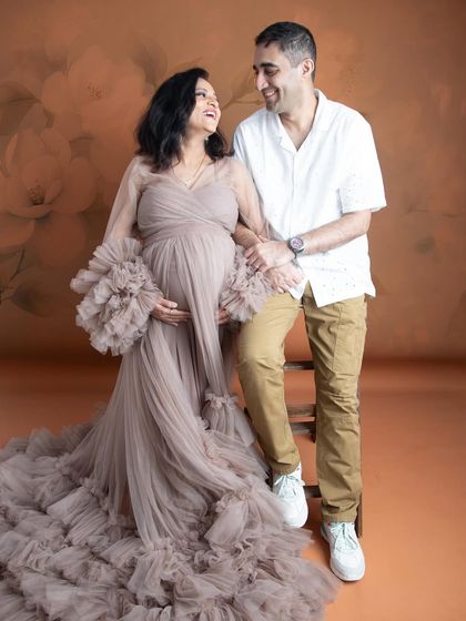 A happy and relaxed couple's portrait. The mom-to-be looks radiant in a dusty rose ruffled gown, sharing a laugh with her partner.