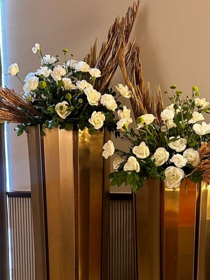 A pair of modern gold vases filled with elegant arrangements of white roses and dried pampas grass. This decor adds a touch of contemporary luxury to any space.
