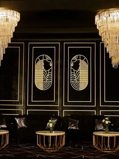 A moody and luxurious Sangeet lounge with a black and gold Art Deco theme, featuring plush seating and magnificent tiered chandeliers.