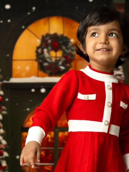 A little girl dressed in a classic red Christmas dress, looking up with wonder at the holiday lights.