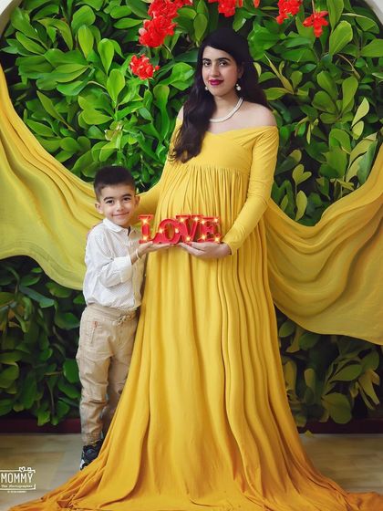 A bright and joyful maternity portrait. The mom to be looks radiant in a flowing yellow gown, and her son is so excited to be a big brother, holding the 'LOVE' sign.