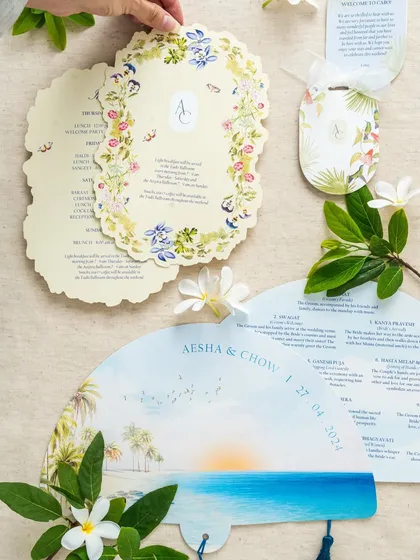 A collection of day-of stationery for a destination wedding, including a fan-shaped program, floral itinerary cards, and welcome bag tags. All pieces are designed with a cohesive visual theme.