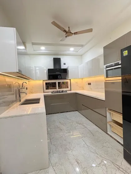 This sleek, modern kitchen features high-gloss cabinets in white and taupe. The handleless design and marble-look flooring create a clean, minimalist, and luxurious feel.