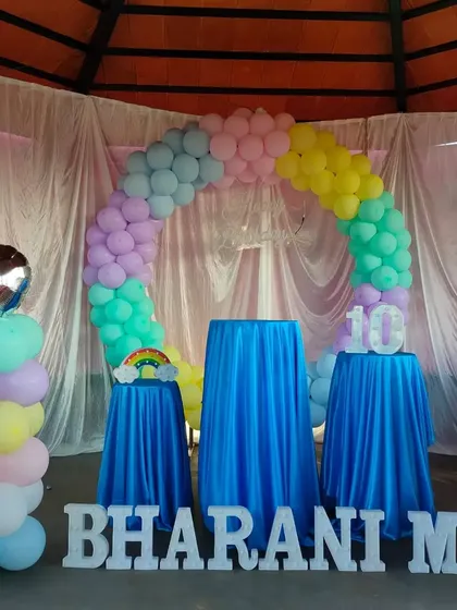 A pastel rainbow balloon arch with blue draped pedestals for a 10th birthday.